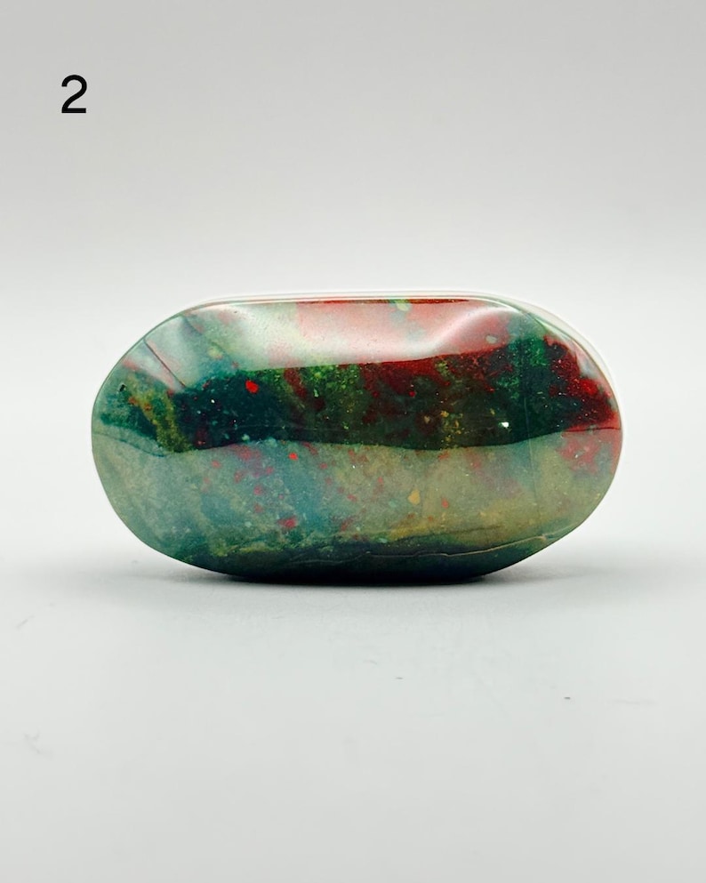 May include: A polished, oval-shaped bloodstone specimen featuring a deep forest green base colour with prominent, irregular patches of vibrant red and subtle hints of yellow and translucent grey throughout the smooth, reflective surface.