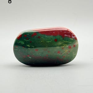 May include: A polished, oval-shaped bloodstone specimen featuring a deep forest green base colour with distinct, scattered bright red spots and patches throughout the surface. The stone has a smooth, glossy texture and is labelled with the number 8.