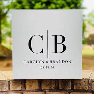 May include: White square sign with black text. The text reads "C|B CAROLYN & BRANDON 08.24.24".