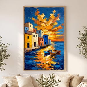 May include: A vertical oil painting in a wooden frame depicting a coastal village with colorful yellow, white, and blue buildings along the water. The sky is filled with vibrant orange and yellow clouds at sunset, reflecting onto the deep blue sea.