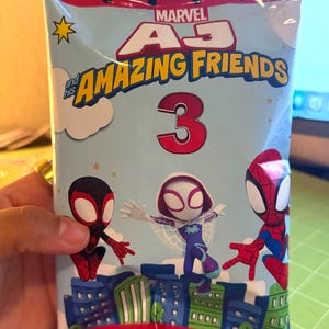May include: A sealed package featuring Marvel's "Amazing Friends" characters. The package has a light blue background with illustrations of Spider-Man, Miles Morales, and Spider-Gwen. The number "3" is prominently displayed.
