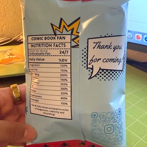 May include: A light blue snack bag with a red top featuring black spider graphics. The bag has text that reads "COMIC BOOK FAN" and "NUTRITION FACTS". The bag also has a speech bubble that says "Thank you for coming!"