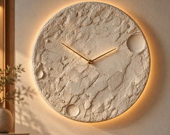 May include: A circular wall clock with a textured, off-white surface resembling the moon's cratered landscape. The clock features thin, gold-colored hands at the center and is illuminated by a warm, soft backlight around its perimeter.