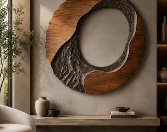 May include: A large circular wall sculpture featuring a combination of smooth, light-toned wood and a dark, deeply textured, carved inner section. The piece has an organic, asymmetrical shape with a hollow center, mounted on a neutral wall.