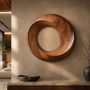 May include: A circular wall sculpture crafted from dark brown wood with a smooth, polished finish. The piece features a continuous, twisted, ring-like form with a hollow center, showcasing natural wood grain patterns throughout its curved surface.