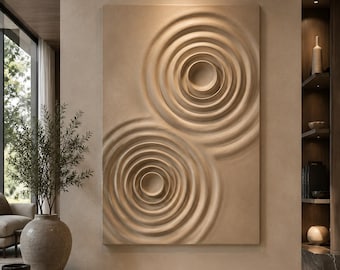 May include: A rectangular wall art piece featuring a beige monochromatic surface with two prominent, raised circular ripple patterns. The design consists of concentric rings that create a three-dimensional effect, resembling water ripples on a flat plane.