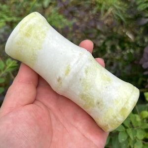 May include: A cylindrical stone object with a smooth, polished surface featuring a marbled pattern of pale yellow and white. The object has a slightly concave center and raised, rounded ends, resembling the segmented appearance of a bamboo stalk.