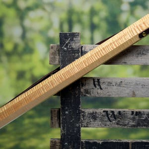 May include: A wooden case with a natural wood finish and brown leather accents. The case is resting on a wooden fence.