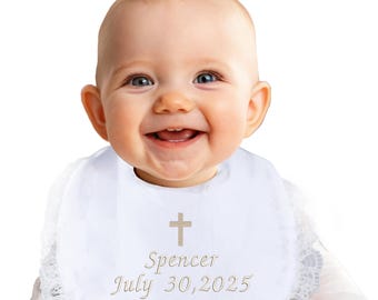 May include: A white baby bib with a lace trim, embroidered with a gold cross, the name "Spencer", and the date "July 30, 2025". The bib is worn by a smiling baby.