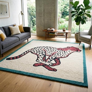 May include: A rectangular area rug featuring a cream-colored background with a large, stylized illustration of a running cheetah in shades of red and black. The rug is framed by a solid teal border, creating a distinct contrast against the light-colored floor.