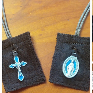 May include: Two black fabric pouches with silver metal charms. The pouch on the left has a blue cross with a silver figure of Jesus Christ. The pouch on the right has a silver oval charm with a blue image of the Virgin Mary. The text on the charm reads "O Mary Conceived Without Sin Pray For Us Who Have Recourse To Thee".