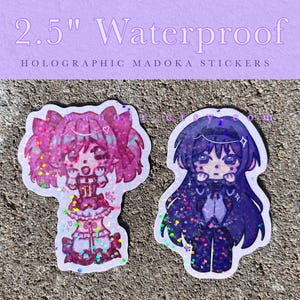 May include: Two 2.5 inch waterproof holographic stickers featuring anime-style characters. One character has pink hair and a pink outfit, while the other has dark purple hair and a dark purple outfit. The text 2.5" Waterproof HOLOGRAPHIC MADOKA STICKERS is visible.
