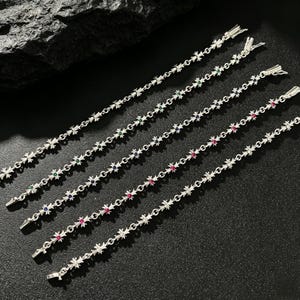 May include: Five silver-toned link bracelets arranged diagonally. Each bracelet features a repeating cross-shaped motif alternating with small, round, faceted gemstones in green, blue, red, and clear white, finished with a metal box clasp closure.