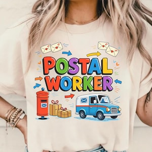 以下が含まれることがあります： POSTAL WORKERという太字のテキストが描かれたカラフルなグラフィック付きのベージュのTシャツ。赤いハートが描かれた白い封筒、赤い郵便ポスト、茶色の小包、青と白の郵便トラックのイラストがデザインされています。