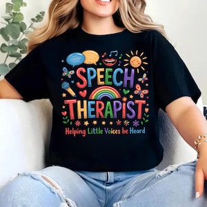 以下が含まれることがあります： SPEECH THERAPISTおよびHelping Little Voices be Heardというカラフルな文字がプリントされた黒いTシャツ。虹、マイク、吹き出し、太陽、蝶、星、花、ハートが様々な明るい色で描かれたデザインです。