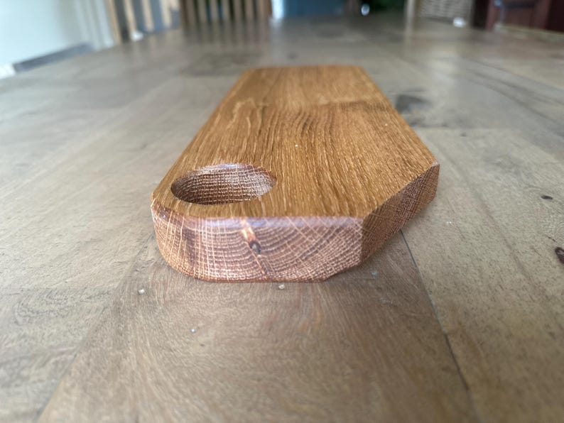 May include: A rectangular wooden serving board with a smooth, light brown finish and a visible natural wood grain pattern. The board features a circular cutout near one end, designed for hanging or handling, with rounded edges and a flat surface.