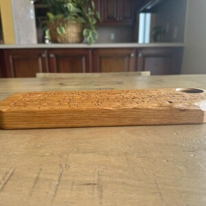 May include: A rectangular wooden serving board with a natural light brown grain and a smooth finish. The board features a single circular cutout near one end, with beveled edges along the corners, showcasing the organic texture of the wood.