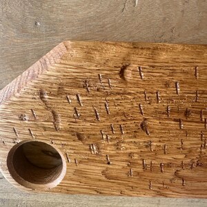 May include: A rectangular wooden serving board with a natural light brown finish and visible wood grain. The board features a circular cutout on the left side and a series of small, vertical, textured indentations across the surface.