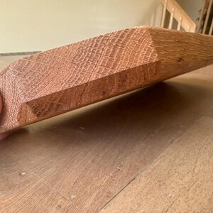 May include: A rectangular piece of reddish-brown oak wood with a visible grain pattern and a beveled edge. The wood block features a smooth, sanded surface texture and a distinct natural wood color, showcasing the dense fibers of the oak material.