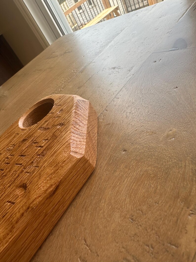 May include: A light brown wooden board with a textured surface and a circular cutout. The board features a beveled edge with visible wood grain patterns and a natural finish, showcasing the raw texture of the wood material in a close-up view.