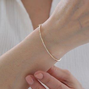 May include: A delicate gold bracelet with small, sparkling accents. The bracelet is curved and wraps around the wrist, showcasing a minimalist design. The bracelet is a beautiful piece of jewellery.