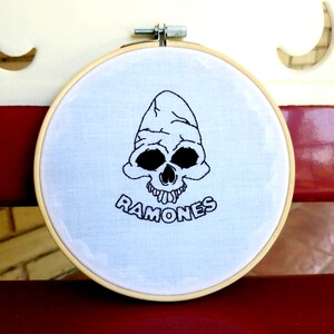 May include: Embroidered hoop art featuring a black and white skull with the word "RAMONES" underneath.