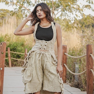 May include: A beige sleeveless waistcoat with a button-up front and a matching high-low skirt featuring ruffled edges, side pockets, and textured patches. The outfit is paired with a black vest top and black ankle boots with a block heel.