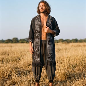 Puede incluir: Una chaqueta larga de color gris oscuro abierta por delante, con un panel vertical ancho de estampado geométrico blanco y flecos en el bajo, combinada con un pantalón holgado de color gris oscuro a juego con puños.