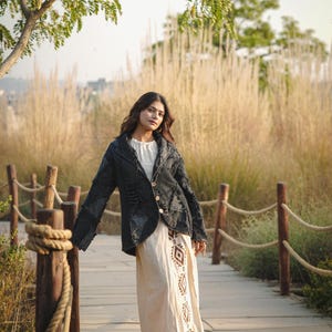May include: A dark charcoal gray textured jacket with a notched collar and three light-colored buttons, worn over a cream-colored long dress featuring a vertical brown geometric pattern along the front panel and black pointed-toe ankle boots.
