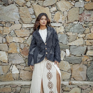 May include: A charcoal gray patchwork blazer with frayed edges and three light-colored buttons, worn over a cream-colored long skirt featuring a vertical brown diamond pattern and a high front slit, paired with black ankle boots.