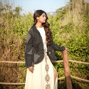 May include: A dark charcoal gray patchwork jacket with distressed textures and visible stitching worn over a cream-colored maxi skirt featuring a vertical row of brown diamond-shaped geometric patterns and a high side slit along the leg.