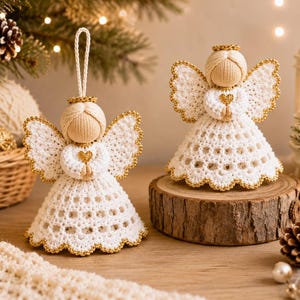May include: Two handmade crochet angel ornaments featuring cream-colored yarn bodies, white lace-like skirts with gold-trimmed edges, and small gold heart accents. One angel has a hanging loop, while the other stands on a round wooden base.