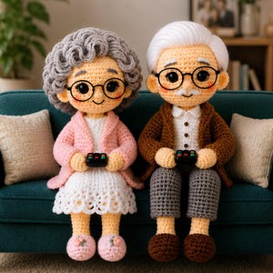 May include: Two crocheted dolls sitting on a teal sofa. The left doll has curly gray hair, pink cardigan, white dress, and pink slippers. The right doll has white hair, brown cardigan, white shirt, and gray pants. Both wear black glasses and hold remotes.