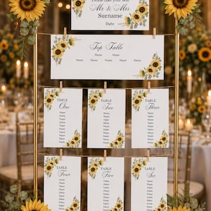 May include: A gold metal frame holding white seating chart cards with sunflower and eucalyptus illustrations. The cards display text including Please take your seat, Mr & Mrs Surname, Top Table, and tables one through six with name placeholders.