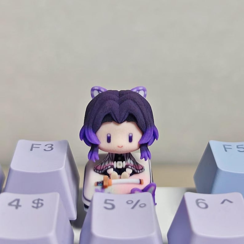 May include: A small, purple-haired figurine with butterfly accents sits atop a keyboard. The figurine has a cute, cartoonish design, with a black and white outfit. The keyboard keys are light purple and blue.