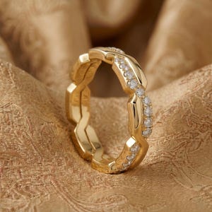 May include: A gold ring with a unique, interwoven design. The ring is adorned with small, sparkling diamonds set along the edges, adding brilliance. The ring's polished surface reflects light, highlighting its intricate details. This piece of jewelry is a statement of elegance.