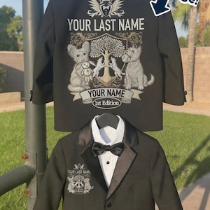 Könnte beinhalten: Ein schwarzer Blazer mit einer großen Grafik auf der Rückseite, die einen Baum, zwei Hunde und den Text YOUR LAST NAME, YOUR NAME sowie 1st Edition zeigt. Ein kleinerer passender Blazer mit weißem Hemd und schwarzer Fliege hängt darunter.