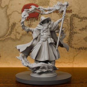 Könnte beinhalten: Eine graue, unbemalte Miniatur aus Kunstharz, die einen Zauberer mit breitkrempigem Hut und langen Gewändern darstellt. Die Figur hält einen hohen Stab in der Hand und ist von wirbelnden magischen Energieeffekten umgeben.