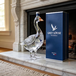 May include: A clear glass bottle shaped like a goose, featuring the Grey Goose Vodka logo and a blue rectangular box with the text Grey Goose Vodka France and a small French flag icon, standing upright with detailed molded feather textures.