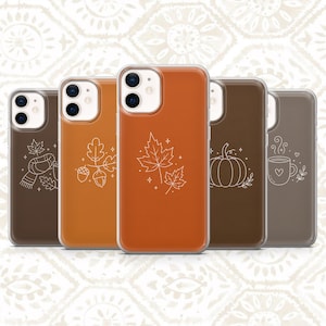 May include: Five smartphone cases in varying shades of brown and orange, each featuring a white line art illustration. Designs include a scarf with leaves, acorns, maple leaves, a pumpkin, and a steaming mug with a heart, all with dual camera cutouts.