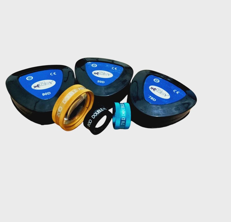 Puede incluir: Un conjunto de tres estuches oft&aacute;lmicos triangulares negros con etiquetas azules marcadas 90D, 20D y 78D, acompa&ntilde;ados de tres anillos circulares para lentes en amarillo, negro y azul, cada uno con texto impreso que indica su potencia di&oacute;ptrica.