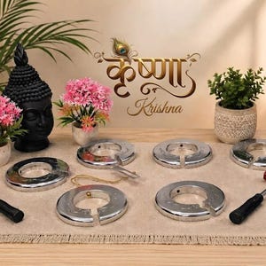 May include: A set of four circular silver-toned metal rings with a split opening, accompanied by two small hammers featuring black handles and red tips. The metal rings have a smooth, reflective surface and are arranged on a light-coloured mat.