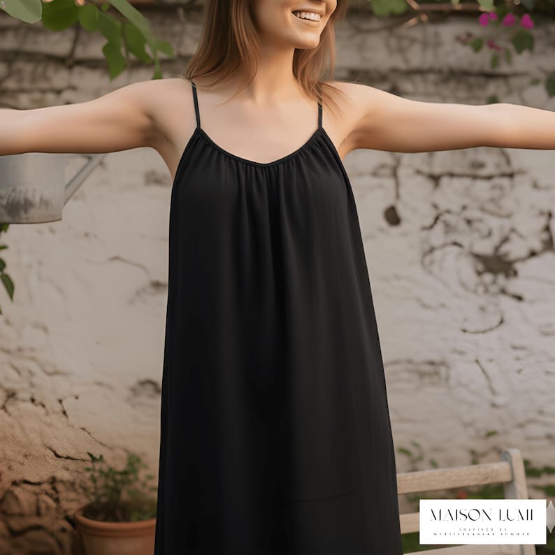 May include: A black slip dress with thin spaghetti straps and a V-neckline. The dress is flowing and appears to be made of a lightweight fabric. The image is set outdoors with a neutral background.