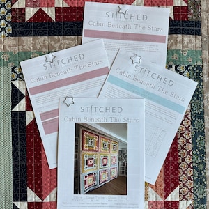 Pode incluir: Quatro folhas de instruções intituladas "Cabin Beneath The Stars" são exibidas em um edredom de patchwork colorido. As folhas são presas com clipes em forma de estrela. O edredom apresenta vários padrões geométricos em vermelho, rosa e azul.