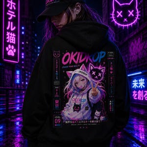 Op de afbeelding: Zwarte hoodie en pet met "OKIDROP" tekst en anime-stijl graphics. De achterkant van de hoodie heeft een kat-thema ontwerp met Japanse tekst en een karakter illustratie. De neonreclames op de achtergrond dragen bij aan de stedelijke esthetiek.