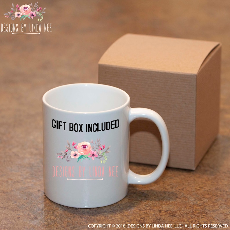 May include: White ceramic mug with a floral design in pink and gray, with the text "GIFT BOX INCLUDED". The mug is accompanied by a brown gift box. The text "DESIGNS BY LINDA NEE" is also visible.