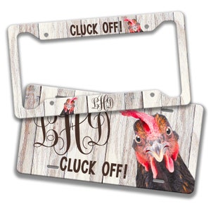 Op de afbeelding: Witte houten kentekenplaatframe met een kippenkop en de tekst "Cluck Off!" in bruine letters. Het frame is ook versierd met een monogram van de letters "BHD" in bruin.