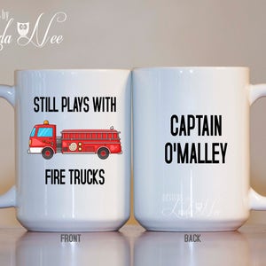 Peut inclure: Une tasse &agrave; caf&eacute; en c&eacute;ramique blanche avec une illustration de camion de pompiers rouge et le texte "Still Plays With Fire Trucks" sur le devant. Le dos de la tasse porte le texte "Captain O'Malley".