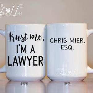 K&ouml;nnte beinhalten: Wei&szlig;e Keramik-Kaffeetasse mit schwarzem Text, der auf der Vorderseite "Vertrau mir, ich bin Anwalt" und auf der R&uuml;ckseite "Chris Mier, Esq." lautet.