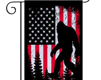 Puede incluir: Una bandera de jardín negra con un diseño de bandera estadounidense desgastado y una silueta de Bigfoot caminando por un bosque.